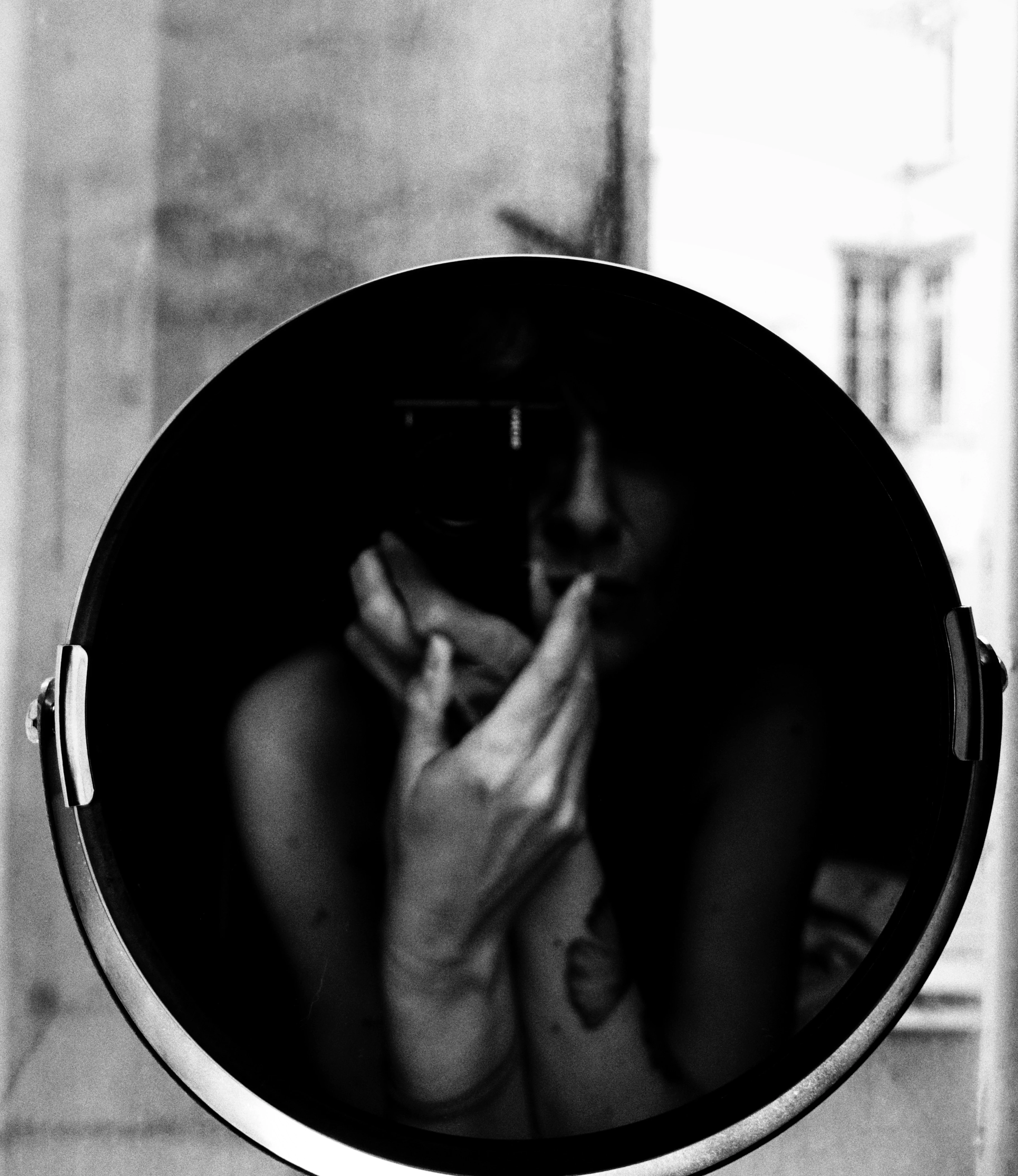 Autoportrait : un bras se reflète dans un miroir rond près d'une lampe d'atelier, noir et blanc
