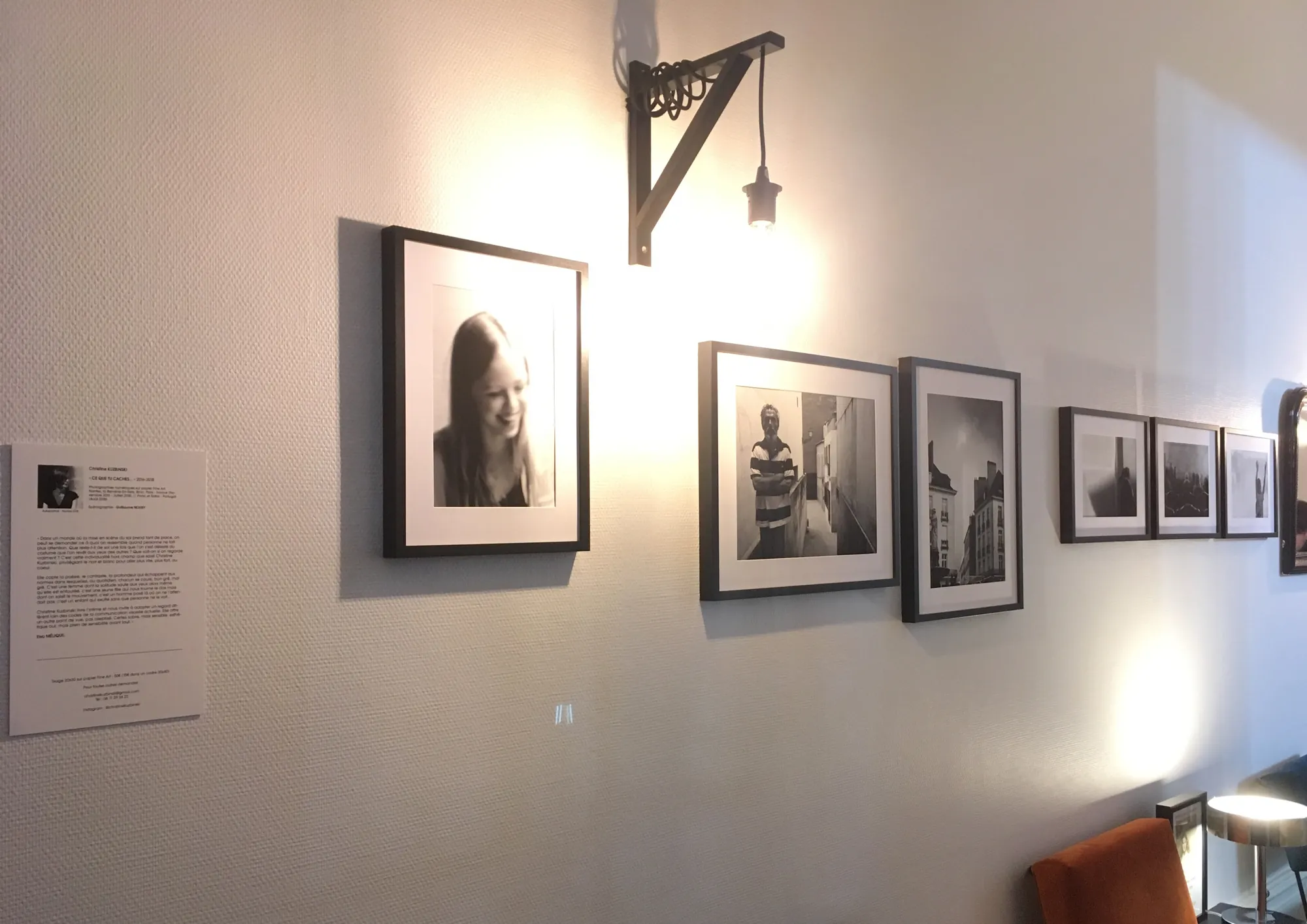 Ce que tu caches… : photographies noir et blanc encadrées, accrochées sous une applique, à côté du texte de présentation